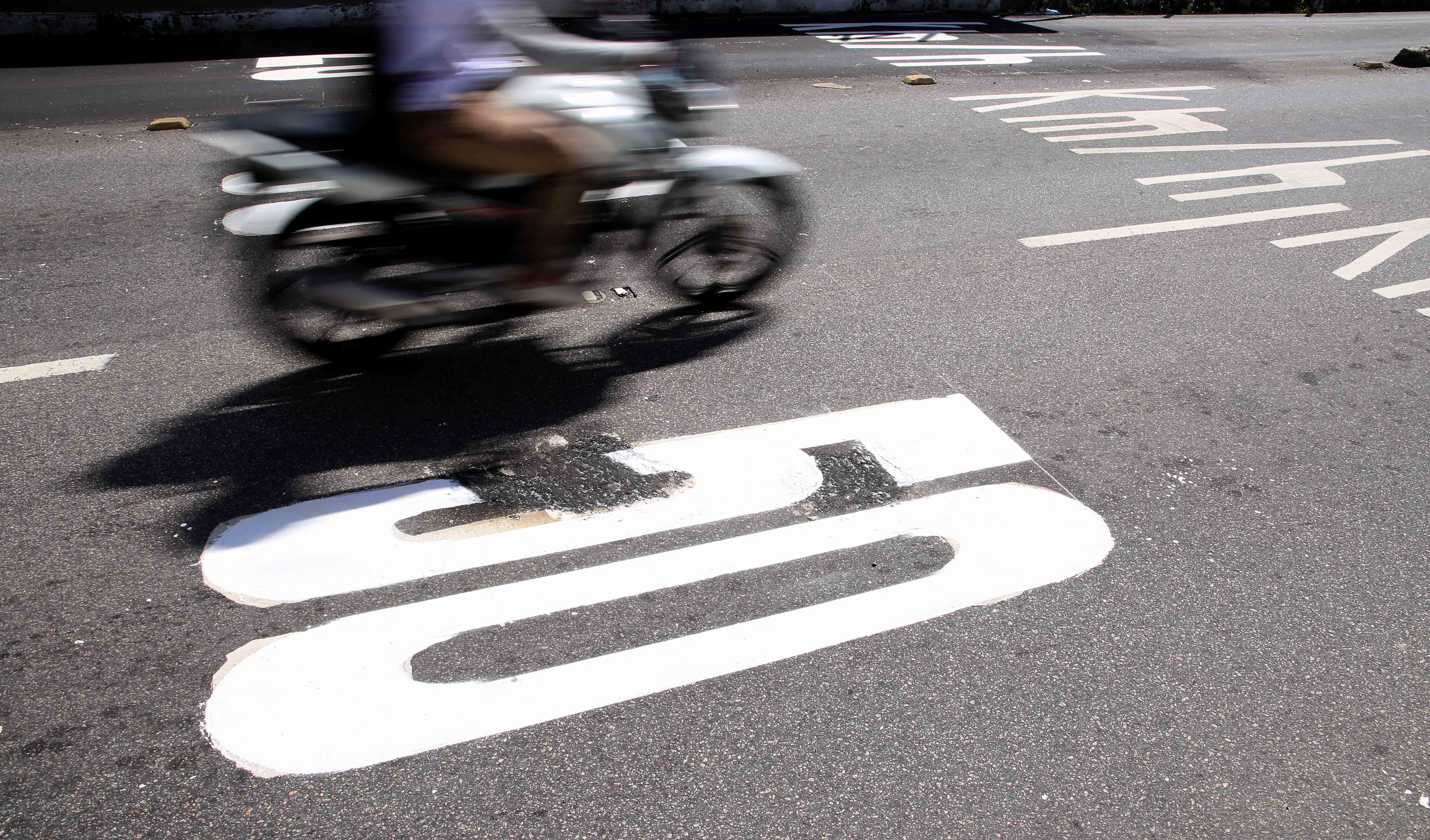 a foto mostra uma moto passando pela sinalização de limite de velocidade de 50km/h pintada no asfalto